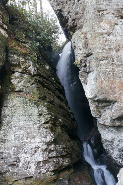 A waterfall cascades down rocky cliffs, surrounded by lush greenery and moss-covered stones.