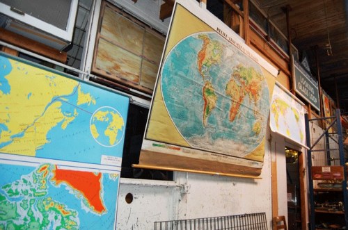 A collection of world maps displayed on a wall in a workshop, showcasing different geographical regions.