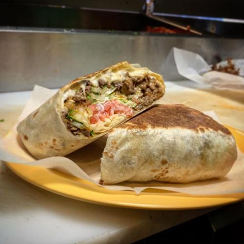 A close-up of a burrito cut in half, revealing beef, cheese, lettuce, and tomato, served on a yellow plate.