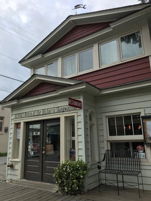 Exterior of a quaint bistro with a sign reading "OUTLAW'S BISTRO at the Historic Skagway," featuring a porch and flower pot.