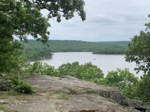 A scenic view of a lake surrounded by lush green trees and hills under a cloudy sky.