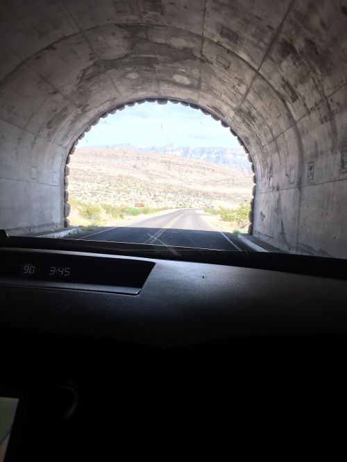 View from inside a tunnel, looking out at a scenic landscape with mountains and a clear sky.