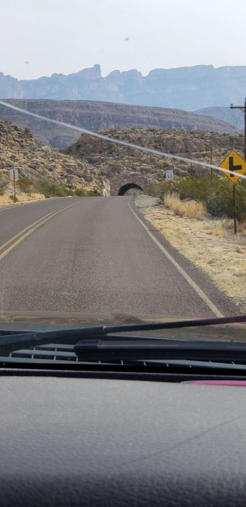 A view of a winding road leading to a tunnel, with mountains in the background and a warning sign ahead.