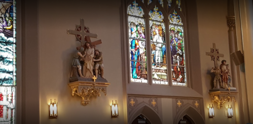 Interior of a church featuring stained glass windows and sculptures of Jesus carrying the cross.