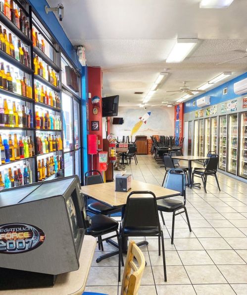 Interior of a convenience store with colorful drink displays, tables, and a view of the checkout area.