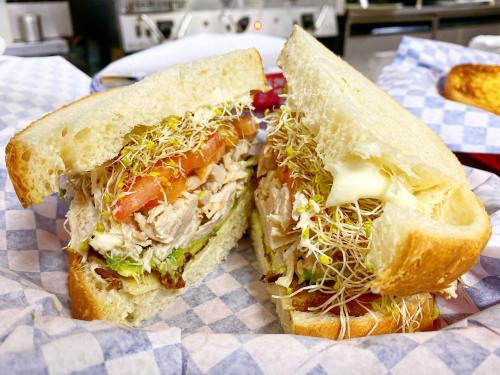 A close-up of a sandwich with turkey, lettuce, tomato, sprouts, and mayonnaise, served on sliced bread.