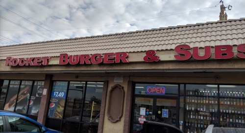 Sign for "Rocket Burger & Subs" with an open sign, featuring a storefront with drinks displayed.