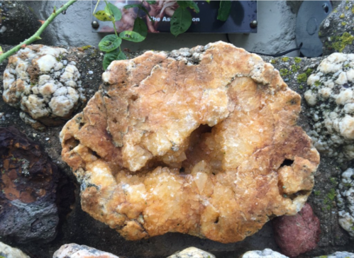 A large, rough stone with a golden-brown hue, featuring crystalline formations and a textured surface.
