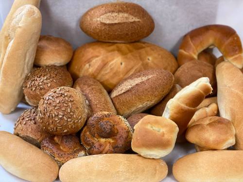 A variety of freshly baked breads, including rolls, loaves, and breadsticks, arranged on a white surface.