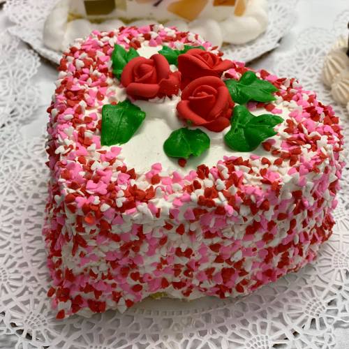 A heart-shaped cake decorated with pink and red sprinkles, topped with fondant roses and green leaves.