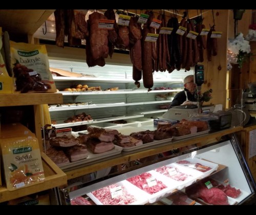 A butcher shop display with various meats hanging above and fresh cuts on the counter, with a worker in the background.
