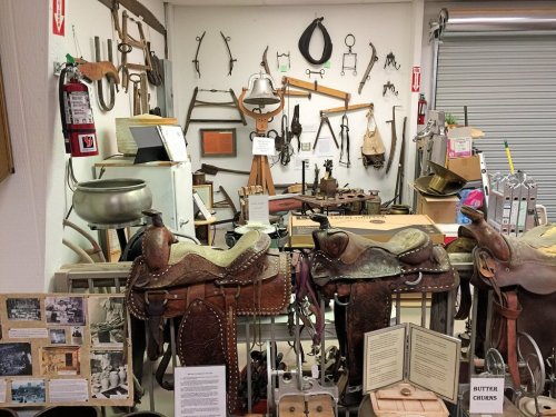 A collection of vintage tools and saddles displayed in a museum, with various artifacts and information boards.