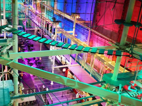 A vibrant indoor space with colorful lighting, featuring elevated walkways and tables below.