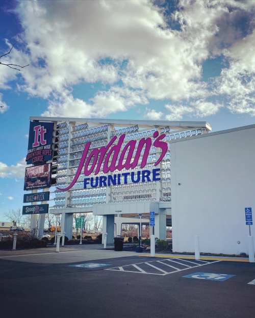 Sign for Jordan's Furniture with a blue sky and clouds in the background, featuring a parking lot in the foreground.