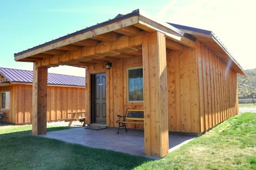 A small wooden cabin with a porch, featuring a door and a bench, set in a grassy area under a clear blue sky.