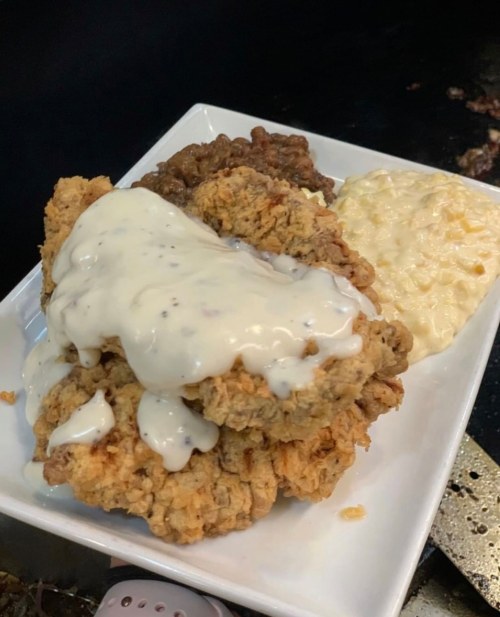 A plate of crispy fried chicken topped with creamy gravy, served with sides of macaroni and cheese and baked beans.