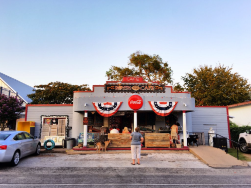 A quaint café with patriotic decorations, featuring a Coca-Cola sign and people enjoying the outdoor seating.