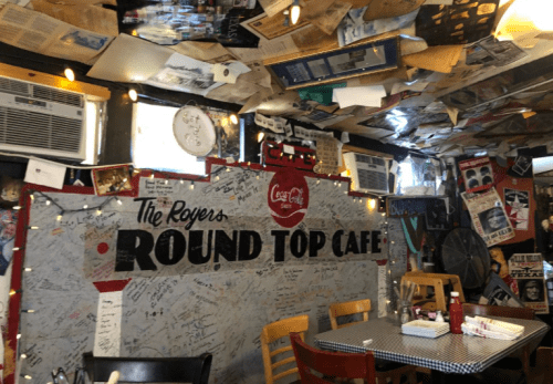 Interior of a cozy café with a wall covered in signatures and memorabilia, surrounded by vintage decor and warm lighting.