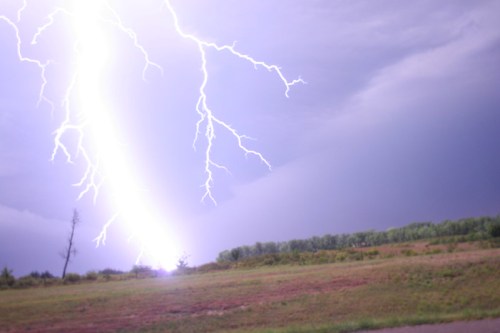 A dramatic lightning strike illuminates a stormy sky over a grassy landscape.