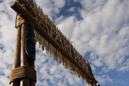Sign for a park made of wood and rope, with a cloudy blue sky in the background.