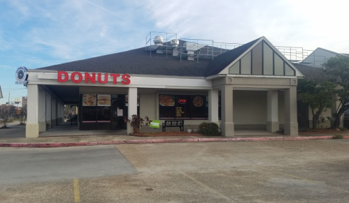 A storefront with a large "DONUTS" sign, featuring glass windows and a parking lot in front.