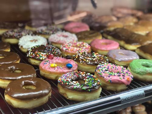 A variety of colorful donuts with sprinkles, chocolate glaze, and frosting displayed on a rack.