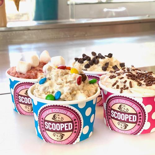 Four colorful cups of cookie dough topped with various sprinkles, chocolate chips, and marshmallows.