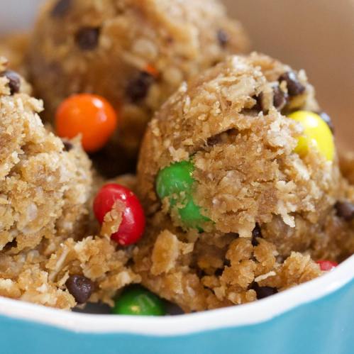 Close-up of cookie dough balls with chocolate chips and colorful candy pieces, in a light blue bowl.