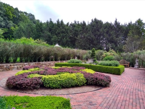 A landscaped garden featuring colorful shrubs, stone pathways, and lush greenery in the background.