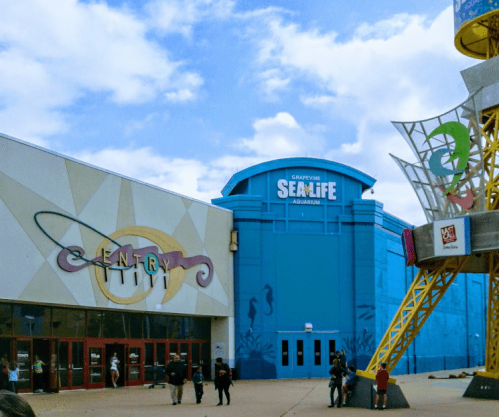Entrance to the Grapevine Sea Life Aquarium, featuring a blue building and colorful signage under a cloudy sky.