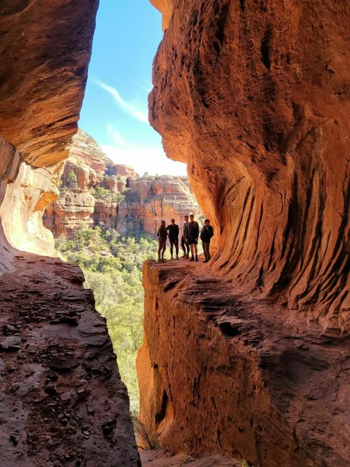 Silhouettes of four people standing on a rocky ledge between two canyon walls, with a blue sky above.