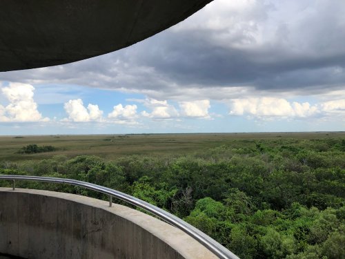 View from a circular observation deck overlooking a vast green landscape and cloudy sky.
