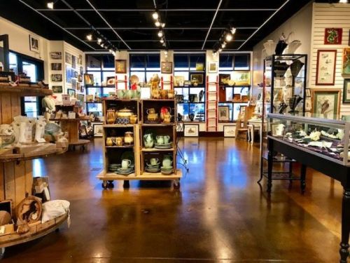 A cozy shop interior filled with various decorative items, artwork, and display shelves on polished wooden floors.
