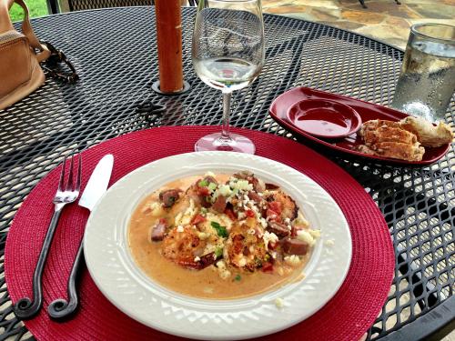 A plate of shrimp dish with sauce, garnished with herbs, alongside a glass of wine and a small plate of bread.