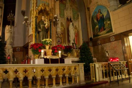 Interior of a church featuring a decorated altar with statues, candles, and festive greenery.