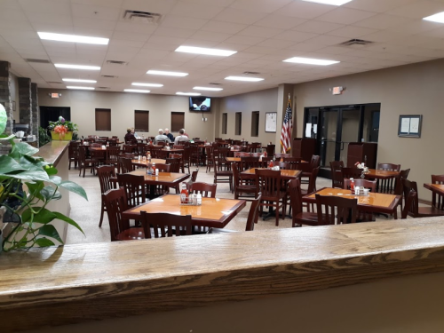 A spacious restaurant interior with wooden tables and chairs, featuring a few diners and an American flag on display.