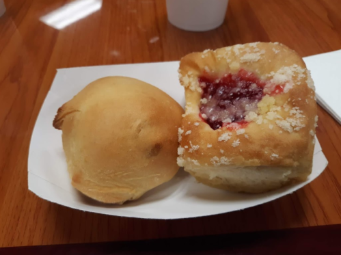 Two baked goods on a white paper plate: one round and golden, the other a sweet roll with a jam filling and sugar topping.