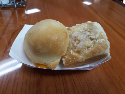 A plate with a soft bread roll and a square pastry topped with crumbly sugar.