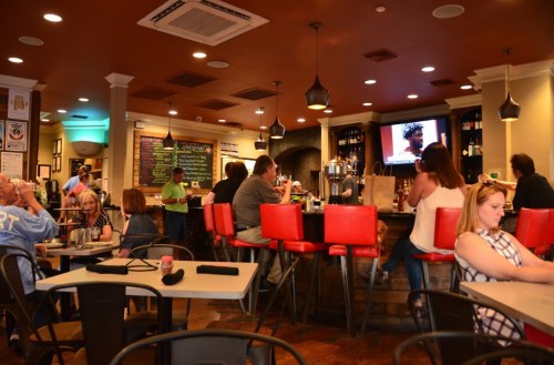 A lively restaurant scene with patrons at the bar and tables, watching a TV and enjoying their meals.