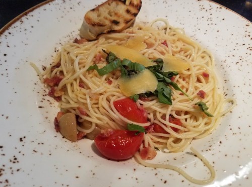 A plate of spaghetti with cherry tomatoes, basil, and garlic, garnished with a slice of toasted bread.