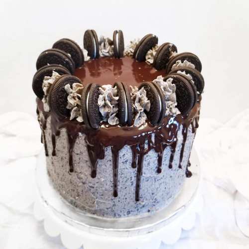 A chocolate cake topped with Oreo cookies and chocolate ganache, decorated with whipped cream swirls.