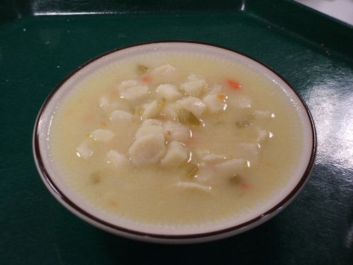A bowl of creamy soup with small dumplings and diced vegetables on a green tray.