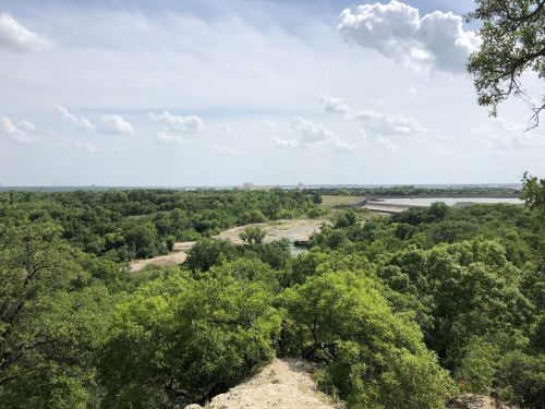 A panoramic view of lush green trees and a river, with a cloudy sky in the background.
