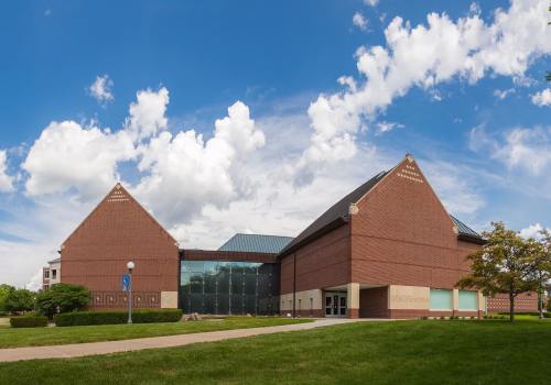 A modern brick building with a glass entrance, surrounded by green grass and under a blue sky with fluffy clouds.