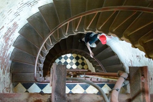 A person in a red cap descends a spiral staircase with a checkered floor pattern below.