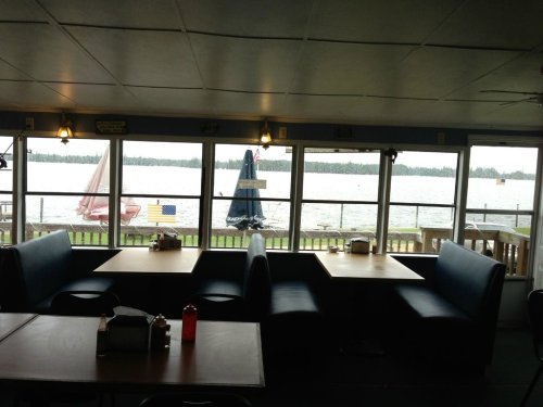 Interior of a lakeside restaurant with empty booths and a view of sailboats on the water through large windows.