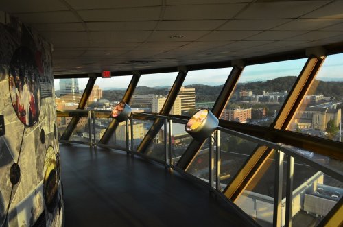 Interior view of a modern building with large windows showcasing a city skyline and mountains in the background.