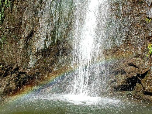 A waterfall cascading over rocks, creating a mist with a faint rainbow visible in the spray.