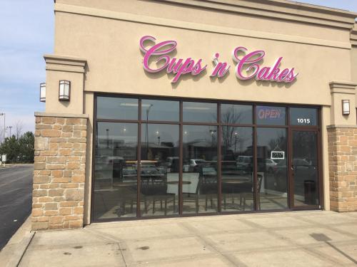 Exterior of a bakery named "Cups 'n Cakes," featuring large windows and an "OPEN" sign.