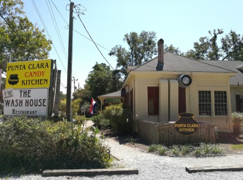 A quaint restaurant with a sign reading "Punta Clara Kitchen" and "The Wash House," surrounded by greenery.